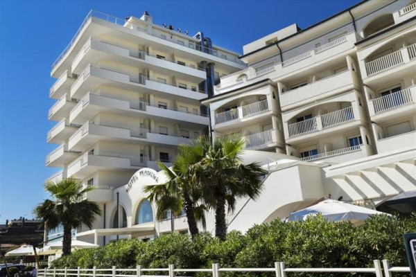 Moderný hotel s balkónmi a palmami v popredí pod modrou oblohou.