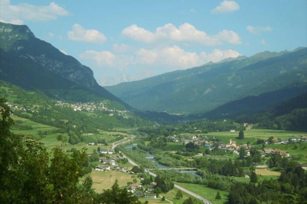 Údolie s dedinami, riekou a horami v pozadí.