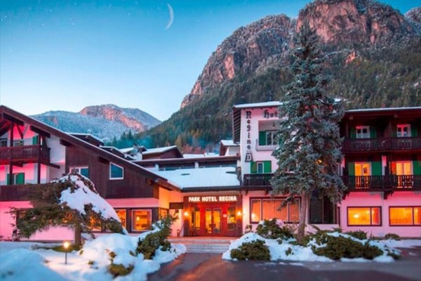 Hotel obklopený zasneženými horami a stromami pri súmraku.
