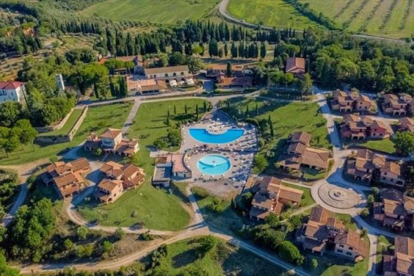 Rekreačné stredisko s bazénmi obklopené zeleňou a domami z vtáčej perspektívy.  