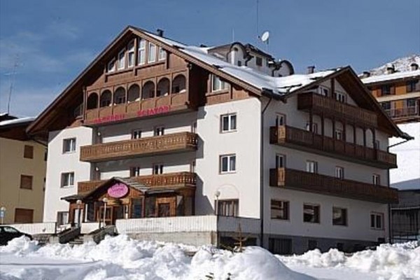 Alpský zasnežený hotel s drevenými balkónmi pod modrou oblohou.
