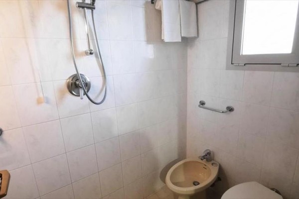 Kúpeľňa s bidetom a sprchou na bielych dlaždiciach.