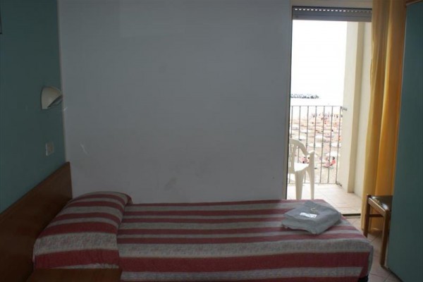 Izba s úzkou posteľou a výhľadom na balkón smerom k pláži.