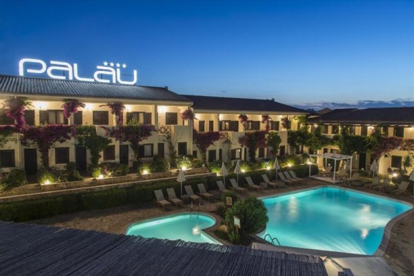 Hotel Palau s bazénom a večerným osvetlením.