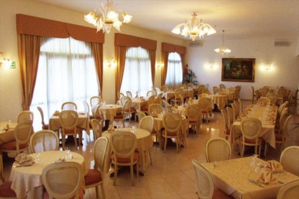 Elegantná reštaurácia s okrúhlymi a obdĺžnikovými stolmi a stoličkami, zdobená lustrami a obrazmi.