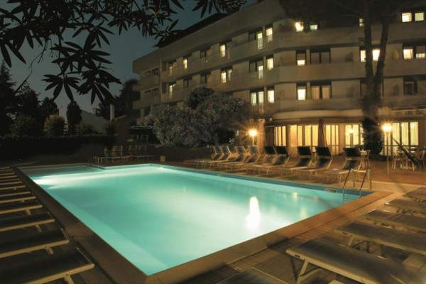 Nočný pohľad na osvetlený bazén obklopený ležadlami pred hotelom.