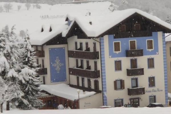 Zasnežený horský hotel s modrými a bielymi fasádami a strechou pokrytou snehom.