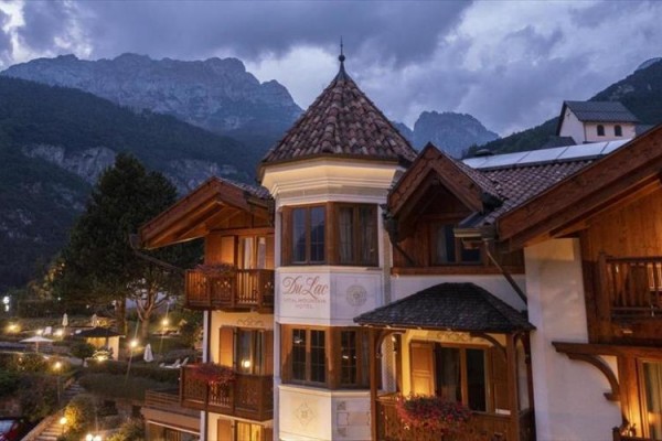 Hotel v alpskej krajine za súmraku s osvetlenými oknami a horským pozadím.