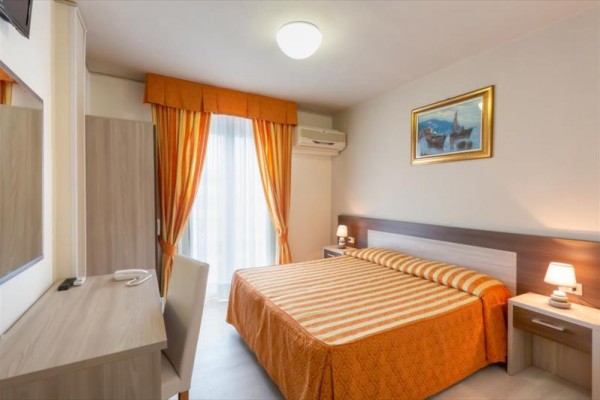Hotelová izba s manželskou posteľou, závesmi a nástennou klimatizáciou.