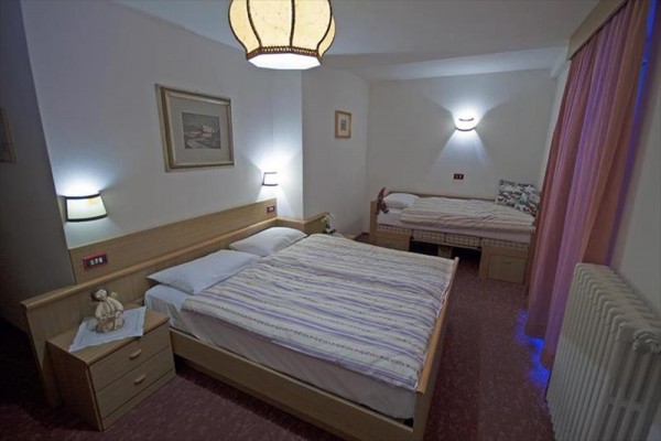 Spálňa s manželskou posteľou a jedným samostatným lôžkom, osvetlená nástennými lampami a svietidlom.