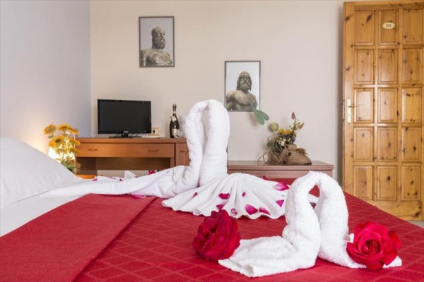 Spálňa s červeným obliečkami, labute z uterákov a ruže na posteli.
