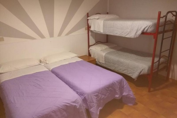 Dve jednolôžka s fialovými prikrývkami a poschodová posteľ v rohu miestnosti s oranžovou podlahou.