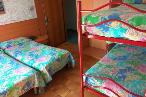 Izba s poschodovou posteľou a dvoma samostatnými posteľami s farebnou posteľnou bielizňou.