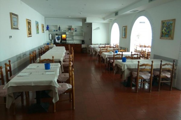 Prázdna reštaurácia s drevenými stoličkami a bielymi obrusmi na stoloch.