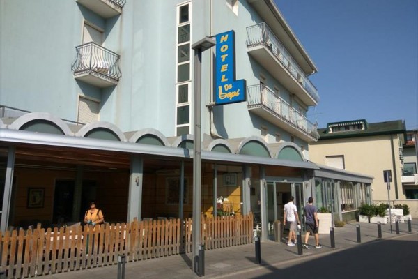 Hotel s modrou fasádou a balkónmi, vchod s nápisom 
