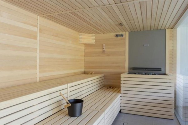 Drevená sauna s lavičkami a pieckou, v rohu vedro a naberačka na vodu.