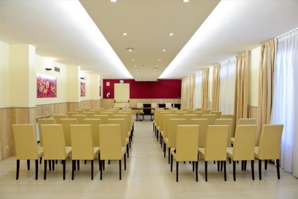 Konferenčná miestnosť s radami béžových stoličiek a prázdnou tabuľou vpredu.