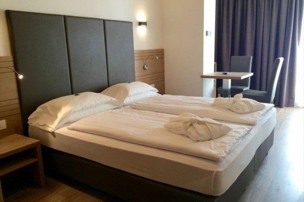 Moderná hotelová izba s manželskou posteľou, písacím stolom a stoličkami.
