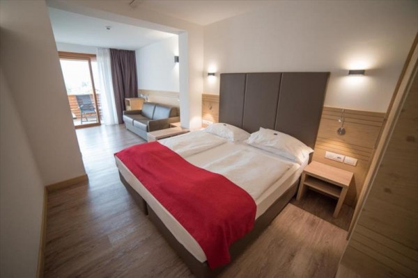 Moderná hotelová izba s manželskou posteľou, pohovkou a balkónom s výhľadom.