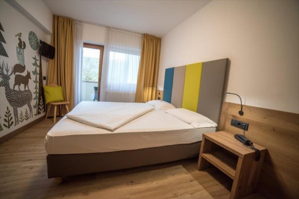 Moderná hotelová izba s manželskou posteľou, nočným stolíkom a maľbou zvierat na stene.