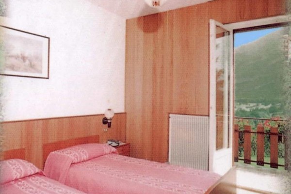 Dve postele s ružovým povlečením v izbe s otvorenými dverami na balkón s výhľadom do prírody.