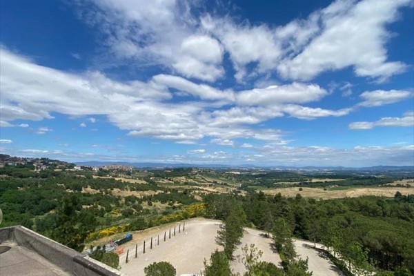 Panoramatický výhľad na krajinu s kopcami, stromami a modrou oblohou s oblakmi.