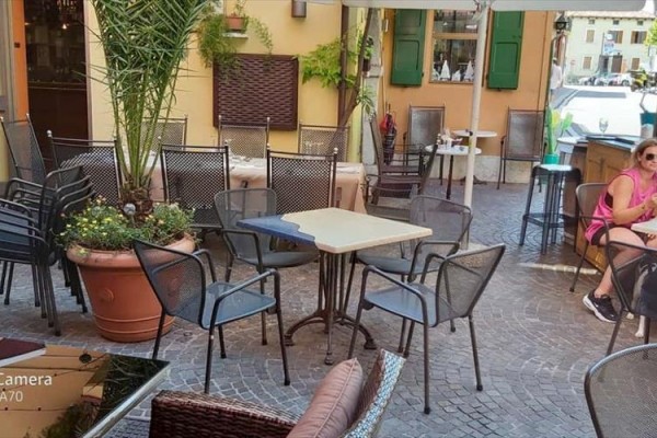 Vonkajšie sedenie kaviarne s prázdnymi stolmi a stoličkami, kde sedí žena v ružovom tričku.