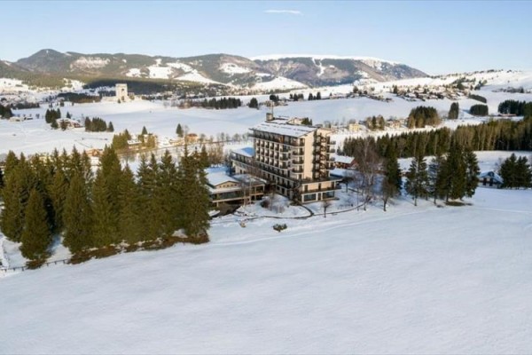 Horský hotel obklopený zasneženou krajinou a lesmi.