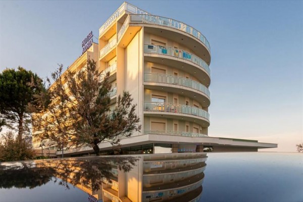 Moderná viacposchodová budova hotela s balkónmi obklopená stromami za súmraku.