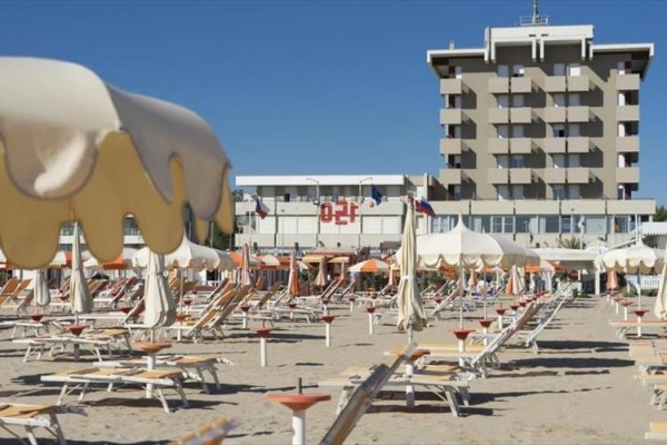 Pláž s ležadlami a slnečníkmi pred vysokým hotelom.