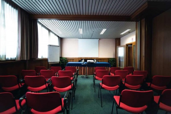 Konferenčná miestnosť s červenými stoličkami a projektorom.