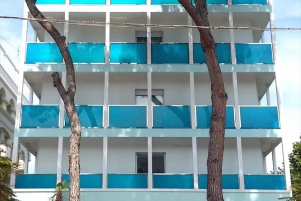 Moderná budova s modrobielymi balkónmi a dvoma stromami v popredí.