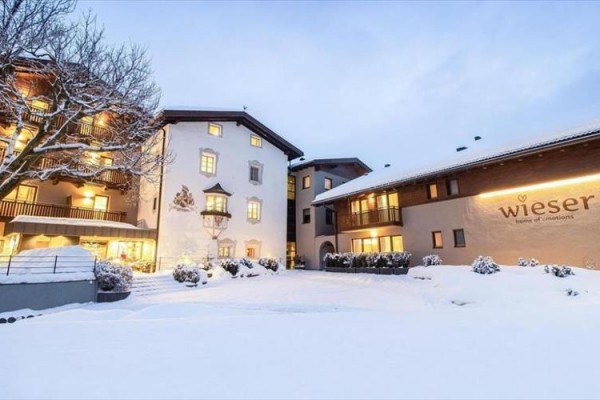 Zasnežený hotel Wieser so zapnutými svetlami a stromami.