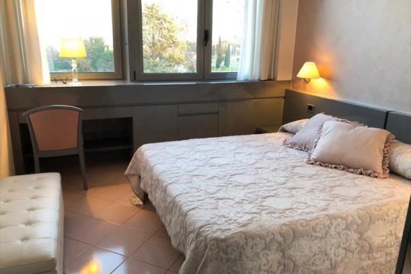 Spálňa s dvojlôžkom, lampami a veľkým oknom s výhľadom do záhrady.