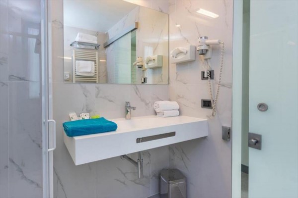 Moderná hotelová kúpeľňa s veľkým zrkadlom a elegantným umývadlom.