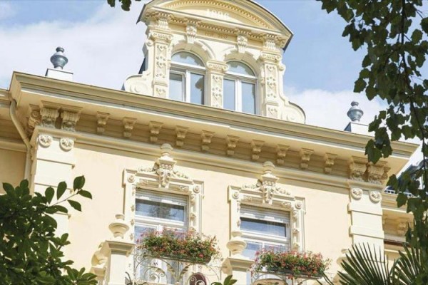 Historická budova s bohatou ornamentálnou fasádou a kvetinovou výzdobou na balkónoch.