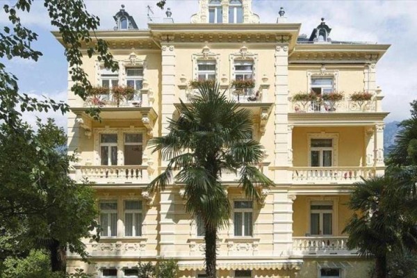 Historická budova so žltou fasádou obklopená palmami.
