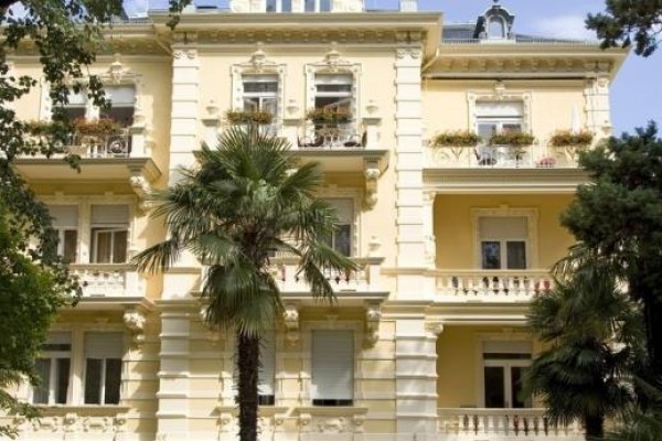 Žltá historická budova s balkónom a palmami v popredí.