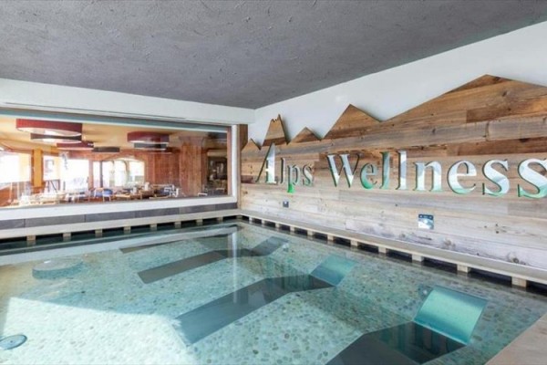 Vnútorný bazén s nápisom Alps Wellness na drevenej stene.
