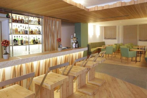 Moderný bar s drevenými stoličkami a lavicami, osvetlený pult s fľašami alkoholu na poličkách v pozadí.