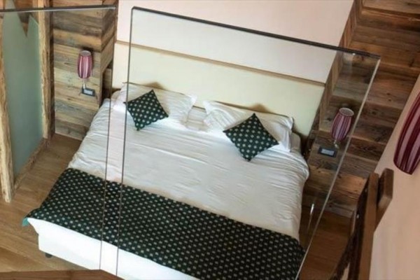 Spálňa s manželskou posteľou, zelenými vankúšmi a drevenými obkladmi na stenách.