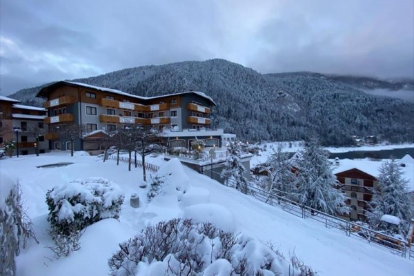 Horský hotel obklopený zasneženou krajinou a lesmi.