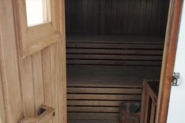 Otvorená drevená sauna s lavicou a malým vedrom vo vnútri.