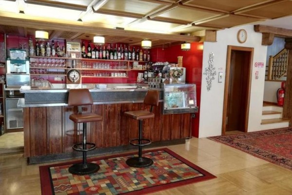 Bar s dreveným pultom, dvoma stoličkami a regálom s fľašami a pohármi.