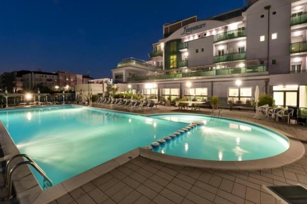 Nočný pohľad na osvetlený hotel s vonkajším bazénom.
