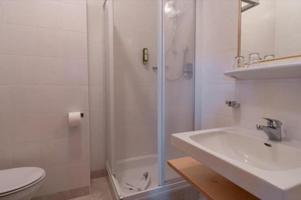 Kúpeľňa so sprchovacím kútom, umývadlom a toaletou na svetlých dlaždiciach.  