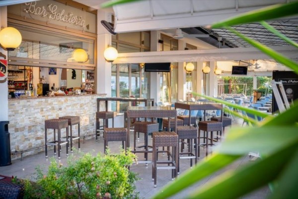 Vonkajší bar s vysokými stolmi a stoličkami, ozdobený lampami a rastlinami.