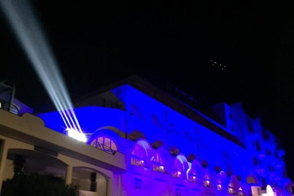 Budova osvetlená modrými svetlami s reflektorom premietajúcim svetlo na oblohu v noci.