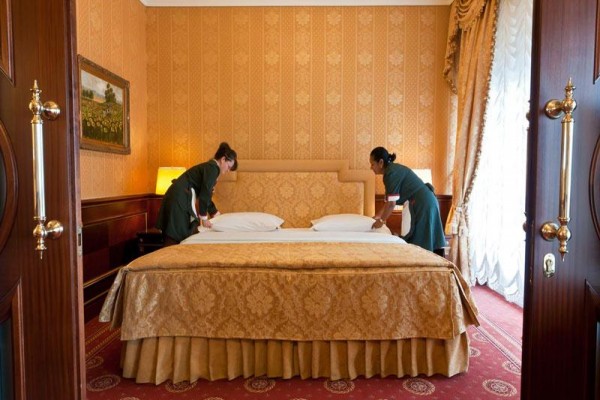 Dve chyžné upravujú manželskú posteľ v luxusnej hotelovej izbe.  