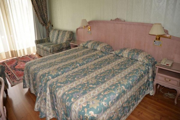 Dve jednolôžkové postele s kvetinovou posteľnou bielizňou v hotelovej izbe s pohovkou a balkónom.